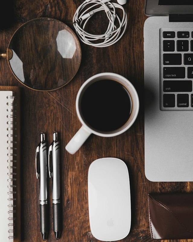 Overhead view of a laptop, a cup of black coffee and a notebook on a desk