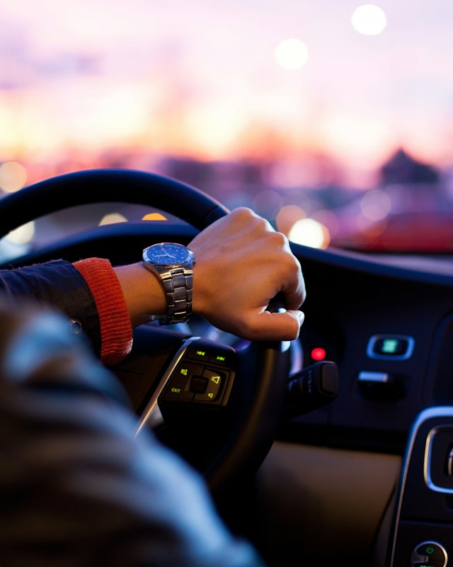 Hands on a steering wheel while driving home at sunset