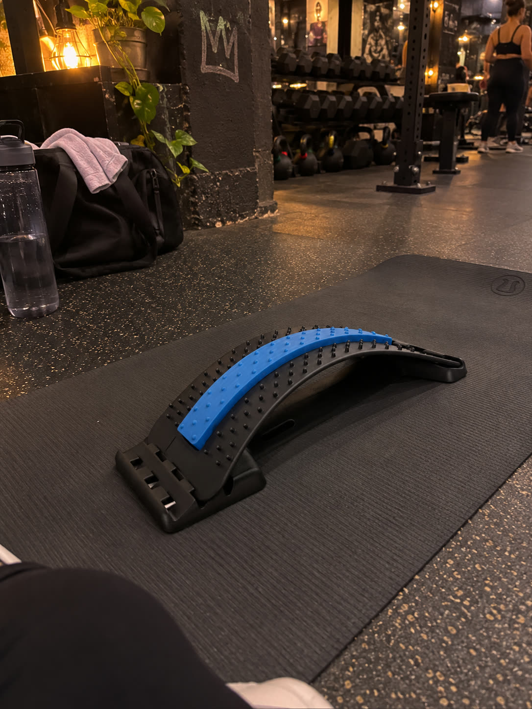 The back stretcher on a yoga mat on a gym floor, a water bottle and gym bag behind it